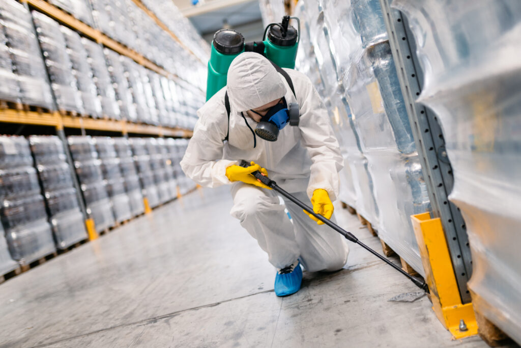 worker in white hazmat suit spraying chemicals inside a facility