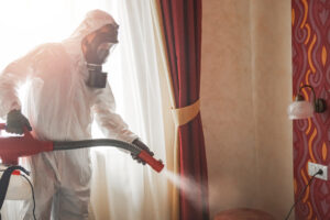 Pest control specialist in white hazmat suit working inside a room