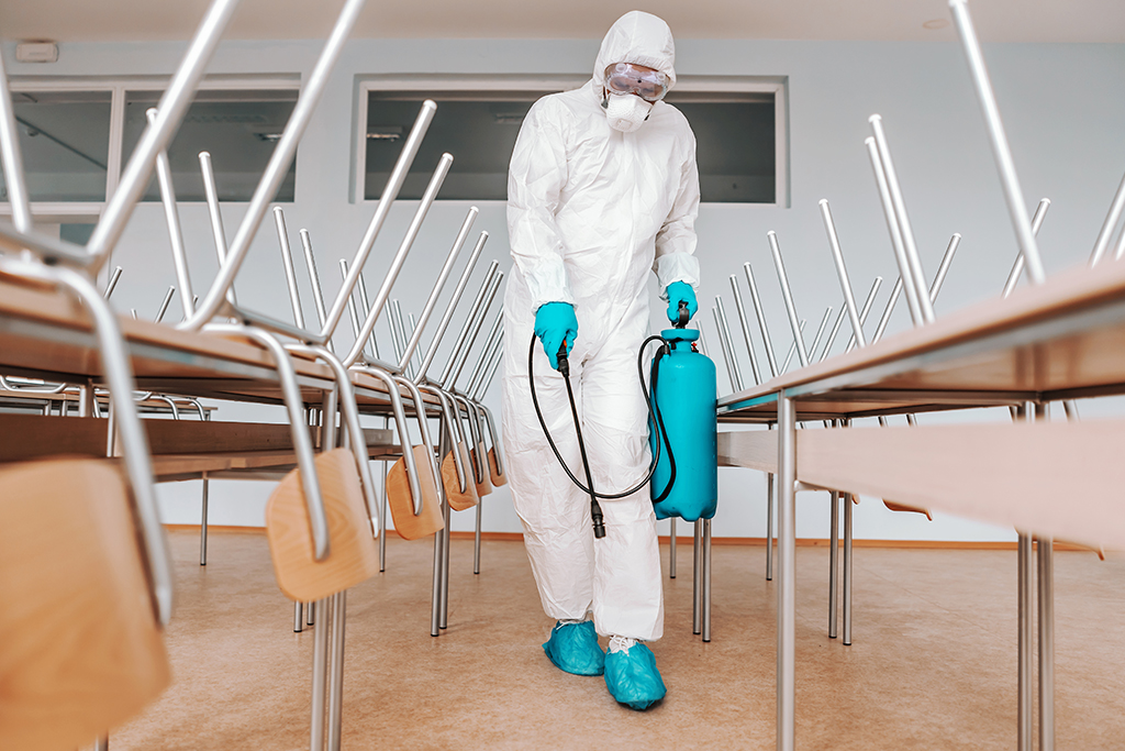 Exterminator in hazmat suit cleaning classroom